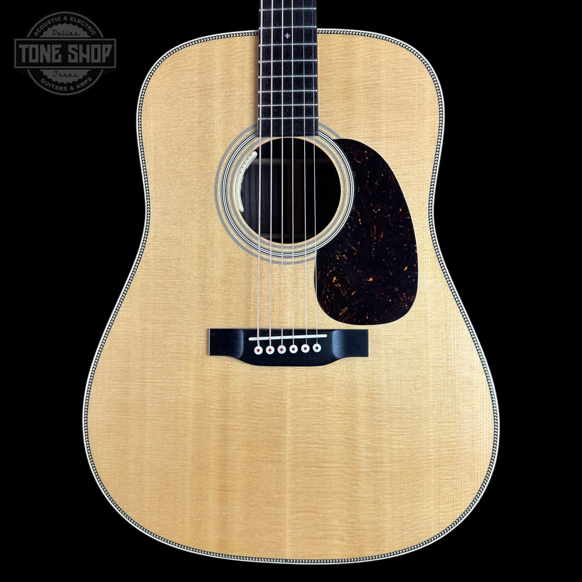 A close-up studio shot of an acoustic guitar body against a solid black background, featuring a natural wood finish, a dark tortoiseshell pickguard, and a black bridge. A circular 'TONE SHOP' watermark is visible in the top left corner.