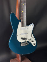 Blue electric guitar with a white pickguard on a dark background