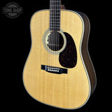 A close-up studio shot of a wooden acoustic guitar body against a solid black background, featuring a natural light-colored spruce top, dark brown sides, a black pickguard, and a white rosette.