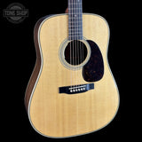 A close-up studio shot of an acoustic guitar body against a solid black background, featuring a natural wood grain top, dark brown sides, and a black pickguard.