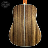 The back of an acoustic guitar with a dark brown and black wood grain finish, featuring a white binding edge and a light-colored neck joint, shown against a solid black background.
