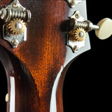 Close-up of the headstock of a guitar, showing the dark brown wood finish, metal tuning pegs, and white tuning keys against a black background.