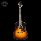 A Taylor acoustic guitar with a classic sunburst finish, shown vertically against a solid black background. The guitar features a dark brown outer edge fading to a warm amber-orange center, with a glossy black pickguard and headstock.