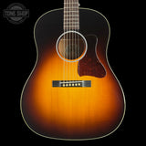 A classic acoustic guitar with a sunburst finish, featuring a bright orange center fading to a dark black edge. The guitar is shown from a front-facing angle against a solid black background, with a Tone Shop watermark in the upper left corner.