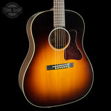 A classic acoustic guitar with a natural sunburst finish, featuring a dark brown outer edge fading to a warm amber-orange center, set against a solid black background.
