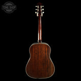 The back of an acoustic guitar with a rich dark brown wood finish, shown against a solid black background with a Tone Shop watermark in the top left corner.