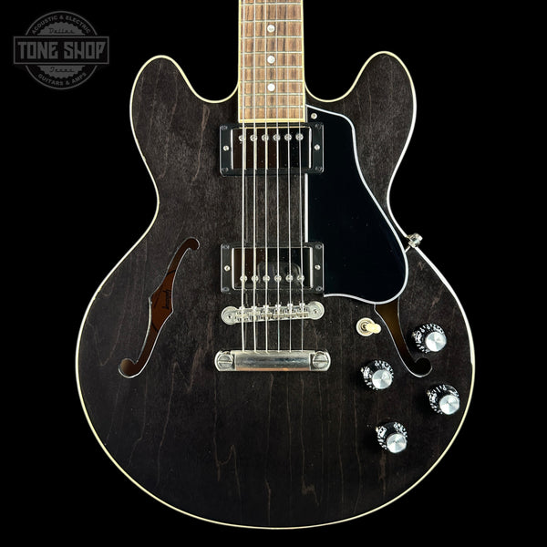 A black electric guitar with a dark wood grain finish, featuring a black pickguard, chrome hardware, and a maple neck, shown against a solid black background.
