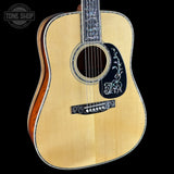 Acoustic guitar with decorative pickguard on a black background, featuring 'Tone Shop' logo.