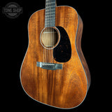 Acoustic guitar with a dark wood finish on a black background, featuring the Tone Shop logo.