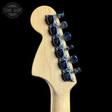Close-up of a guitar headstock with tuning pegs on a black background, featuring the Tone Shop logo.