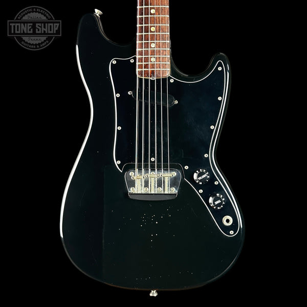 Black electric guitar with a clear coat on a black background, featuring the Tone Shop logo.