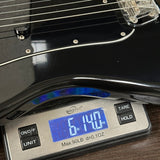 Guitar being weighed on a digital scale with a display showing weight.