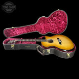 Acoustic guitar in a black case with pink interior on a black background, featuring 'Tone Shop' logo.