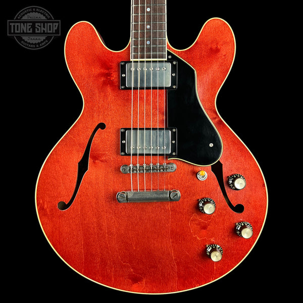 A classic double-cutaway electric guitar with a vibrant red-orange sunburst finish, black pickguard, and chrome hardware, shown against a solid black background with a Tone Shop watermark in the top left corner.