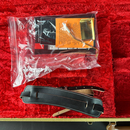 Black guitar strap on a red surface with a clear plastic bag containing accessories.