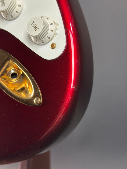 Close-up of a red guitar with control knobs and a gold pickguard on a gray background