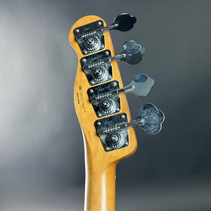 Close-up of a guitar headstock with tuning pegs on a gray background