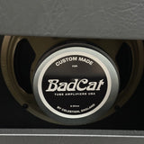 A close-up of a circular speaker center label reading 'BadCat' with 'Custom Made' and 'Tube Amplifiers USA' printed on it, mounted inside a dark gray amplifier cabinet.
