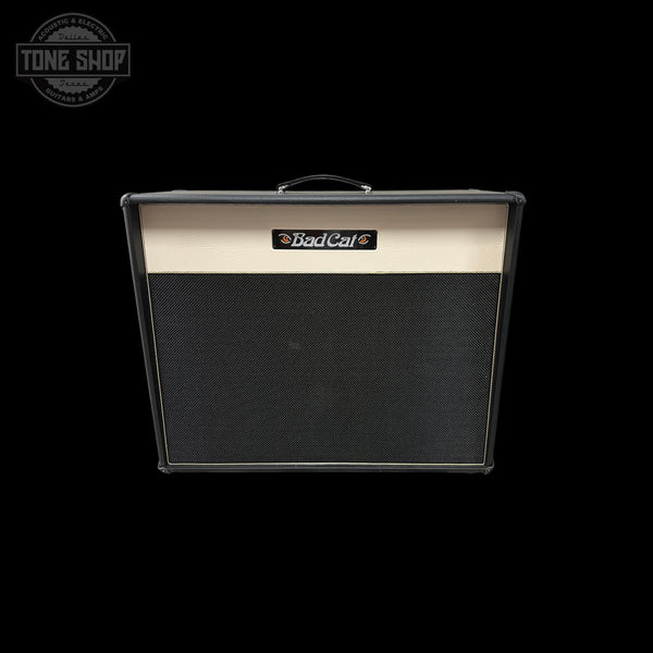 A Bad Cat guitar amplifier cabinet with a black grille and a cream-colored top panel, shown against a solid black background with a Tone Shop watermark in the upper left corner.