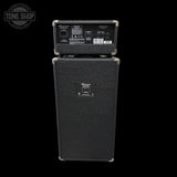 A black Marshall amplifier stack with the head unit resting on top of the speaker cabinet, photographed against a solid black background. The front features a textured black grille with a central Marshall logo badge, and the rear of the head unit is visible showing various input and output connectors.