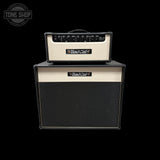A Bad Cat 2x100W guitar amp combo with a cream-colored head and a black speaker cabinet, shown against a solid black background. A Tone Shop watermark is visible in the top-left corner.