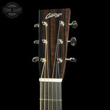 Close-up of a Collings acoustic guitar headstock with six silver tuning pegs and six strings, set against a solid black background.