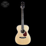 A natural wood acoustic guitar with a dark reddish-brown pickguard, shown vertically against a solid black background. A circular 'TONE SHOP' watermark is visible in the top-left corner.
