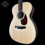 A close-up studio shot of an acoustic guitar body against a solid black background, featuring a natural flamed maple top, dark wood sides, and a decorative rosette.
