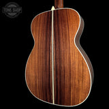 Close-up of the back of an acoustic guitar showing a rich, dark brown wood grain finish with a light cream center stripe and white binding, set against a solid black background.