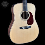 An acoustic guitar with a natural wood finish and dark brown sides, shown against a solid black background. A Tone Shop watermark is visible in the top left corner.