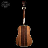 The back of an acoustic guitar with a glossy dark brown wood grain finish, shown against a solid black background with a Tone Shop watermark in the top left corner.