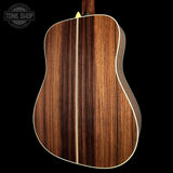 The back of an acoustic guitar with a rich dark brown wood grain finish, featuring a single light-colored center stripe and white binding, shown against a solid black background with a Tone Shop watermark in the top left.