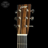 Close-up of the headstock of a Collings acoustic guitar against a solid black background, showing the dark wood grain, six tuning pegs, and six strings. A Tone Shop watermark is visible in the top left corner.