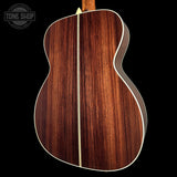 Close-up of the back of an acoustic guitar showing a rich dark brown wood grain finish with a light cream binding, set against a solid black background.
