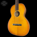 A vintage-style acoustic guitar with a natural sunburst finish, shown against a solid black background. A Tone Shop watermark is visible in the top-left corner.