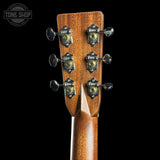 Close-up of the headstock of a wooden acoustic guitar, showing six tuning pegs with decorative metal caps and a glossy brown wood finish, set against a solid black background.
