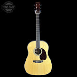 A natural wood acoustic guitar with a dark headstock and pickguard, shown vertically against a solid black background. A circular 'TONE SHOP' watermark is visible in the top-left corner.