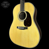 A close-up studio shot of an acoustic guitar body against a solid black background, featuring a natural wood finish, a dark tortoiseshell pickguard, and a black bridge. A Tone Shop watermark is visible in the top-left corner.