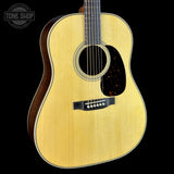 A close-up studio shot of an acoustic guitar body against a solid black background, featuring a natural wood grain top, dark brown sides, and a black pickguard.