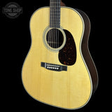A close-up studio shot of an acoustic guitar body against a black background, showing a natural wood finish, soundhole rosette, pickguard, and part of the neck. A Tone Shop watermark is visible in the upper left corner.