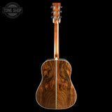 The back of an acoustic guitar with a rich, dark brown wood grain finish, shown against a solid black background with a Tone Shop watermark in the top left corner.