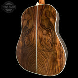 Close-up of the back of an acoustic guitar showing a rich, wavy wood grain pattern in warm brown tones, with a white binding edge, set against a solid black background.