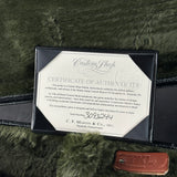 A Martin Custom Shop Certificate of Authenticity document displayed inside a black presentation frame, with a small brown leather FTKL tag nearby on a dark green furry surface.
