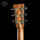 Close-up of the headstock of a wooden acoustic guitar, showing six tuning pegs with decorative black and gold tuners and a Tone Shop logo watermark in the top left corner.
