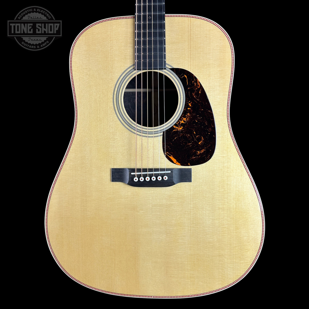 A front-facing acoustic guitar with a natural wood finish, black neck, and a dark tortoiseshell pickguard, shown against a solid black background with a Tone Shop watermark in the top-left corner.