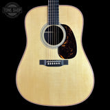 A front-facing acoustic guitar with a natural wood finish, black neck, and a dark tortoiseshell pickguard, shown against a solid black background with a Tone Shop watermark in the top-left corner.