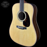 An acoustic guitar with a natural maple top and dark wood sides, shown against a solid black background. A Tone Shop watermark is visible in the top left corner.
