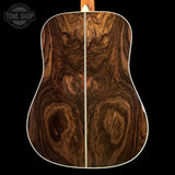 Close-up of the back of an acoustic guitar showing a rich, dark brown wood grain pattern with a white binding edge, set against a solid black background.