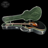 An acoustic guitar with a glossy brown sunburst finish displayed inside an open black hard case with green velvet lining, set against a solid black background.
