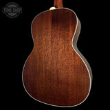 Close-up of the back of an acoustic guitar showing a rich, dark brown wood grain finish and white binding, set against a solid black background with a Tone Shop watermark in the top left.